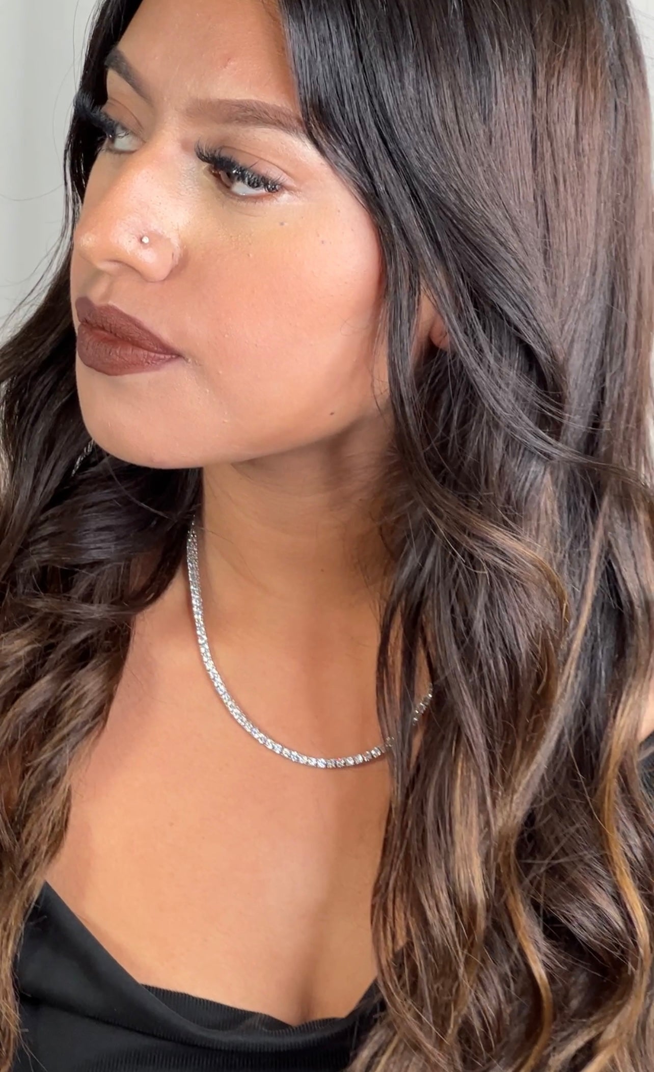 A woman with long wavy hair wearing a black top and Super Silver Cubic Zirconia Tennis Necklace.