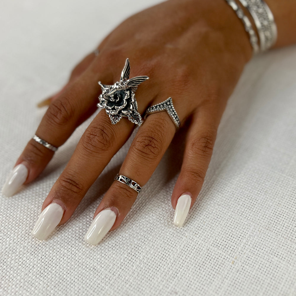 A woman's hand adorned with a delicate Hummingbird with Flower Ring, perfectly contrasting against her white nails reminiscent of delicate flowers in nature.