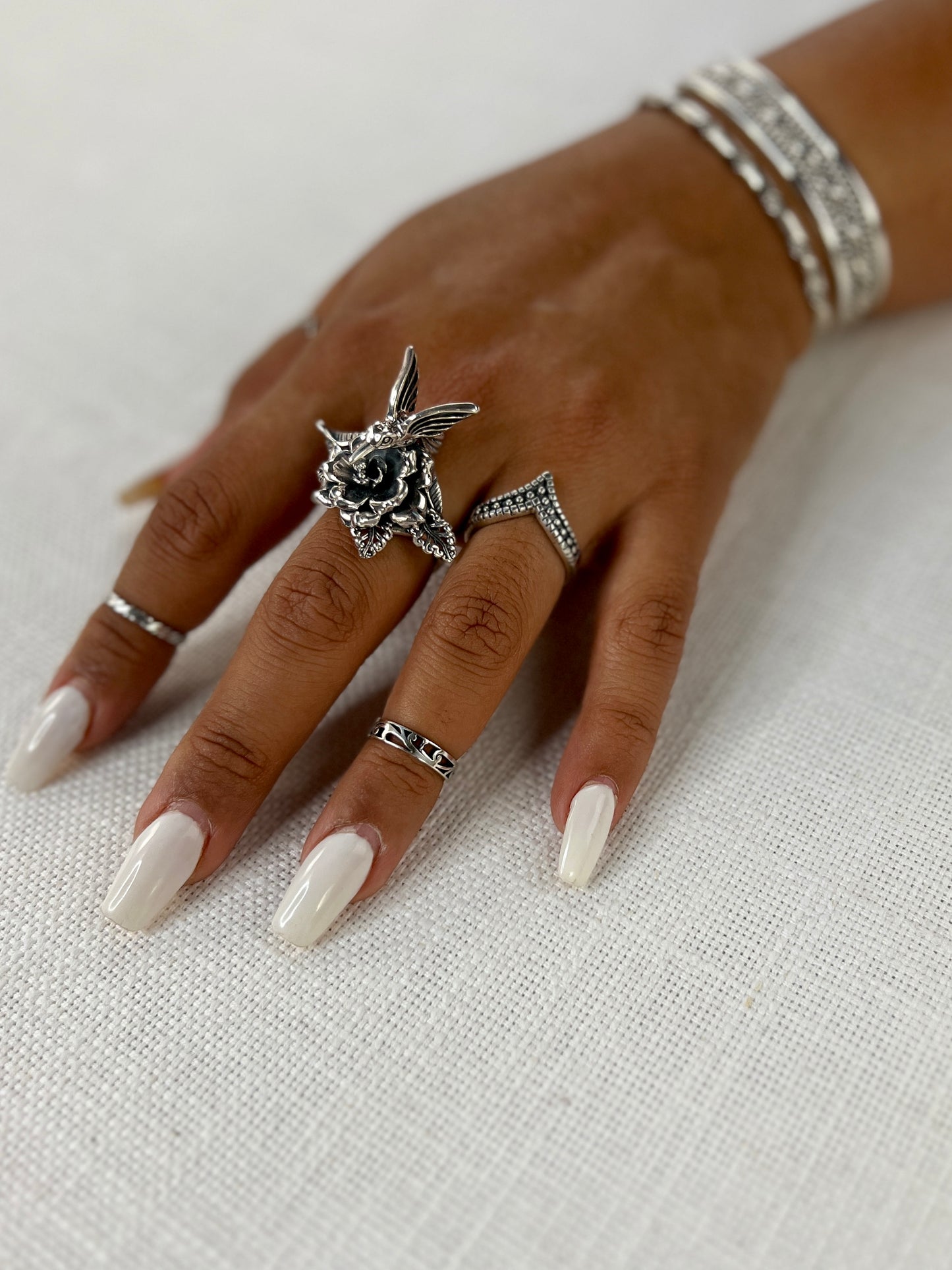 A woman's hand adorned with a delicate Hummingbird with Flower Ring, perfectly contrasting against her white nails reminiscent of delicate flowers in nature.