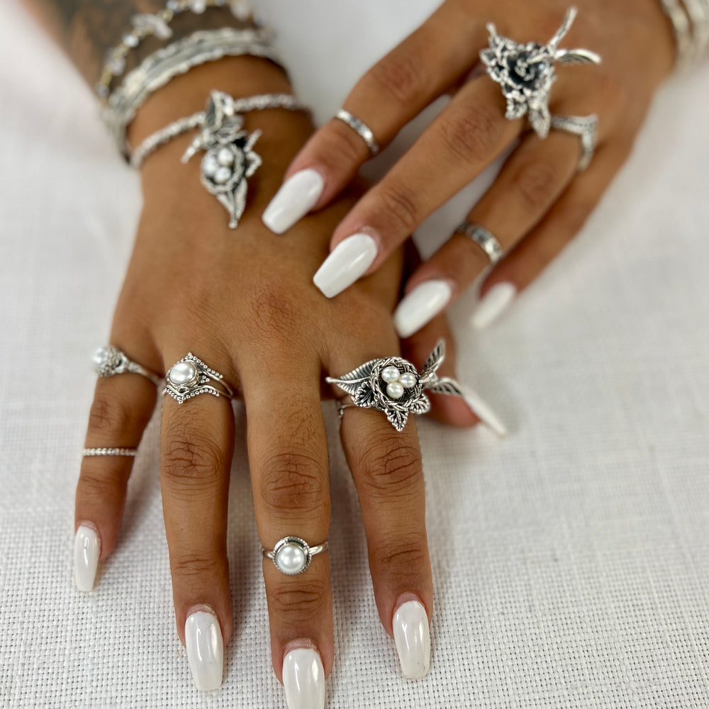 
                  
                    A woman's hands adorned with Super Silver rings, including one with the Hummingbird With Nest of Pearls Ring design, as well as a timeless pearl ring.
                  
                