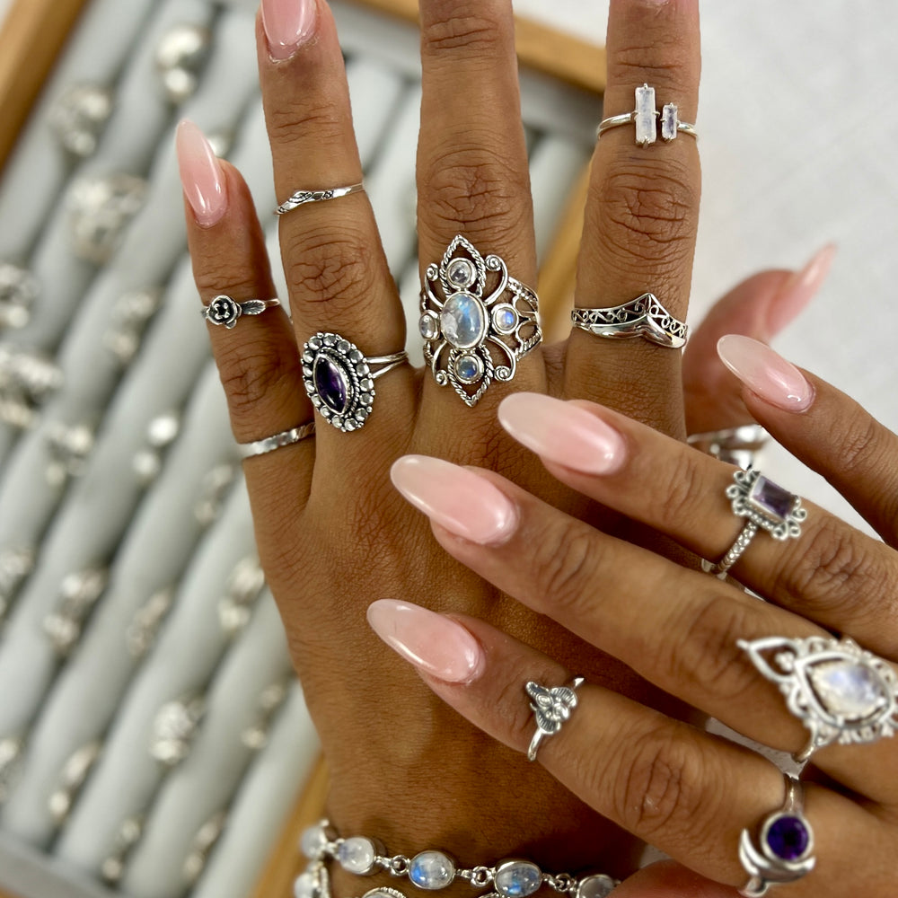 
                  
                    A person's hands adorned with various sterling silver and gemstone rings, including a carnelian and moonstone Online Only Exclusive Multistone Ring, with long pink manicured nails, displayed above a tray of assorted jewelry.
                  
                