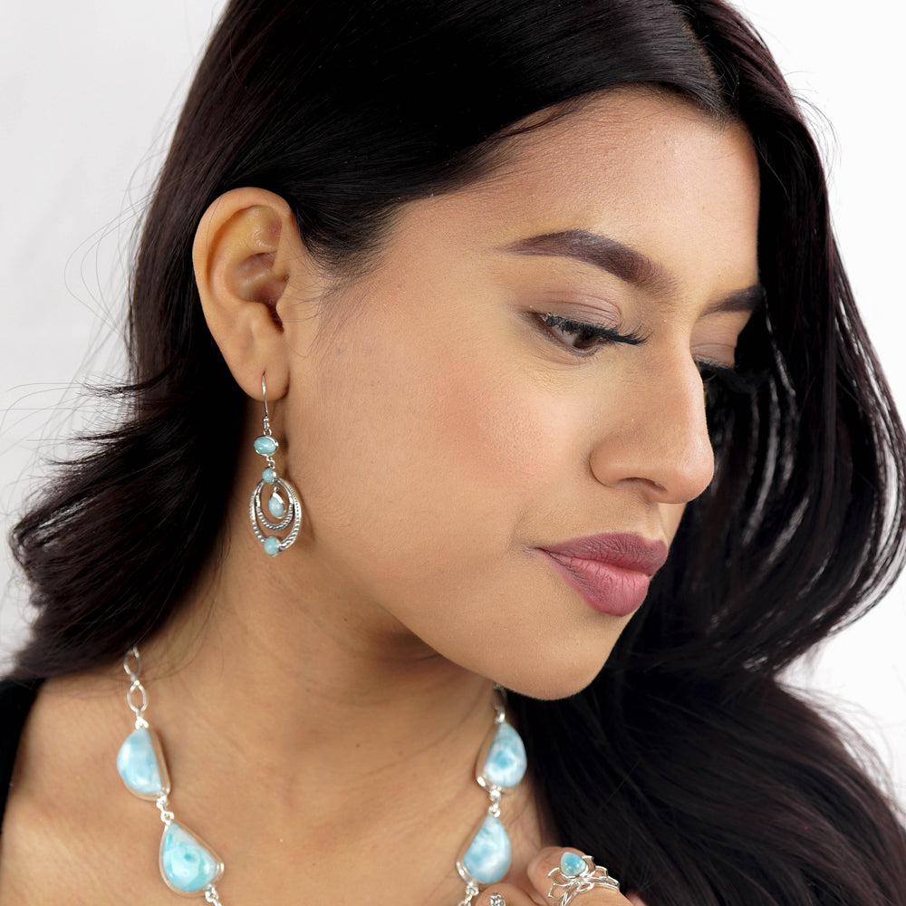 
                  
                    A woman with long, dark hair is shown wearing turquoise jewelry, including earrings, rings, and a Beautiful Larimar Necklace With Teardrop Shape Stones. She is facing slightly to the side against a white background.
                  
                