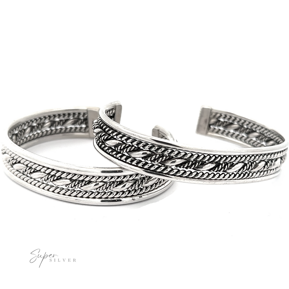 Two intricately designed Native American Handmade Intricate Silver Cuffs with braided patterns displayed side by side on a white background. The bottom left corner features the text "Super Silver." These pieces are reminiscent of Native American craftsmanship, adding a touch of cultural elegance.