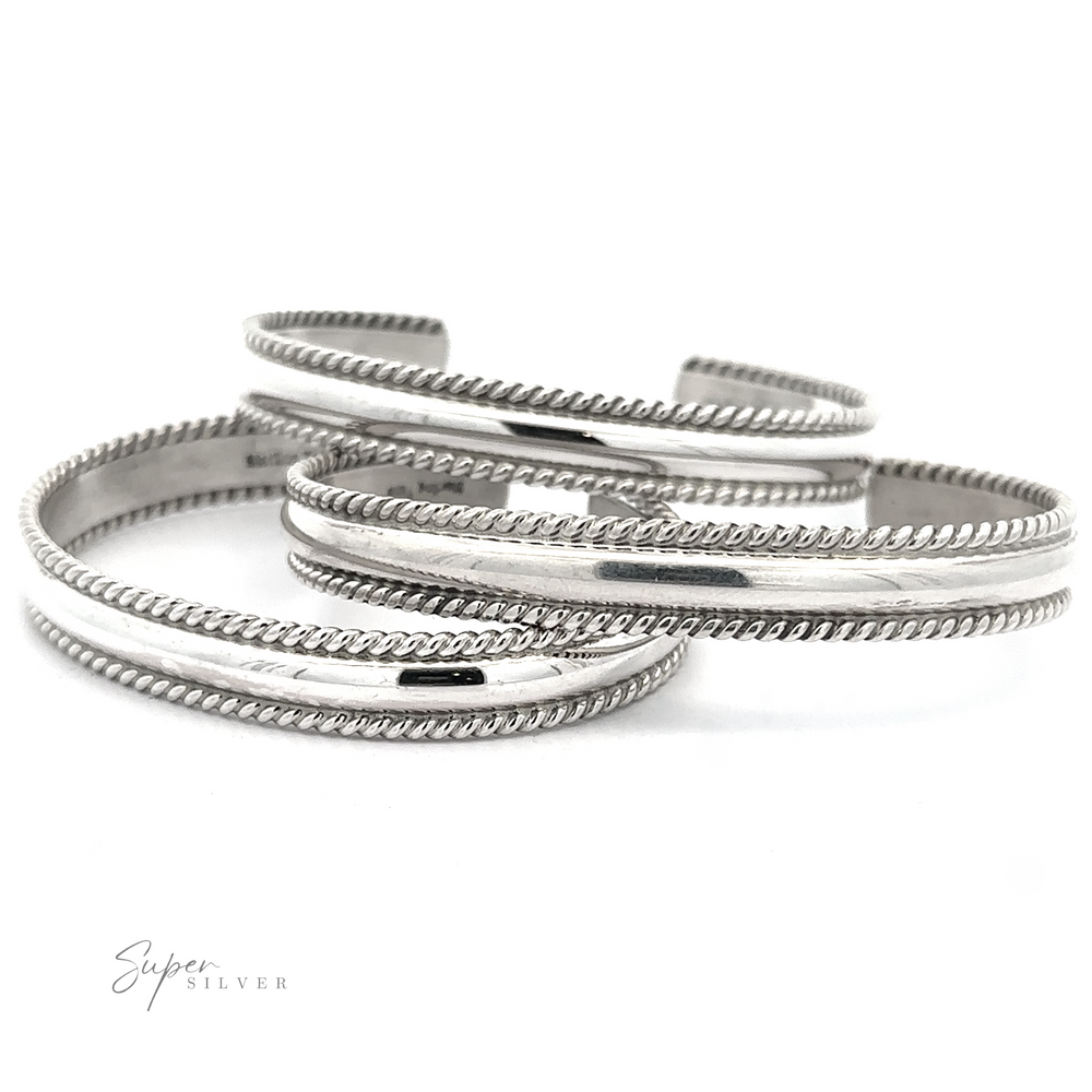 Three polished Native American Handmade Silver Rope Cuffs with rope-like edges, overlapping each other on a white background. The logo 