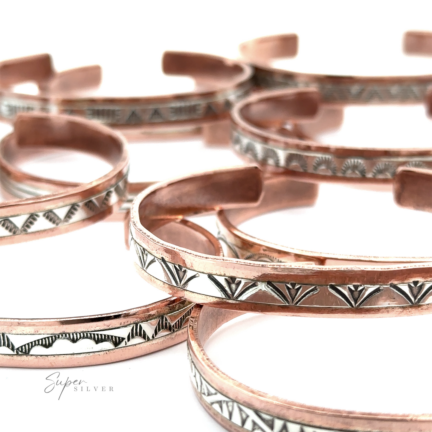 
                  
                    Close-up of several Native American Handmade Copper And Silver Bracelet with sterling silver geometric inlays, arranged in a layered fashion against a white background.
                  
                