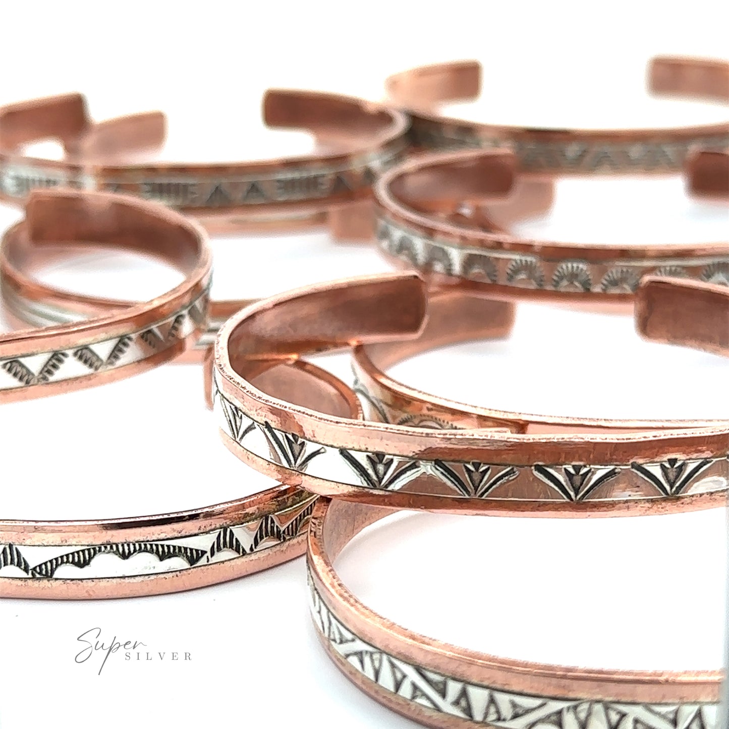 Native American Handmade Copper And Silver Bracelets, featuring etched black and white geometric designs, are arranged in a partially overlapping pattern on a white surface. Some of the pieces incorporate elements of Native American handcrafted artistry.