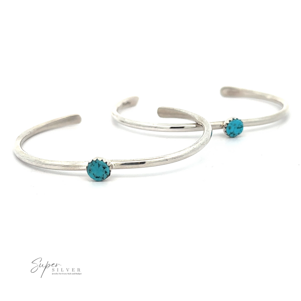 Two silver, minimalist bracelets, each featuring a single Kingman Turquoise stone, are displayed against a white background. The logo 