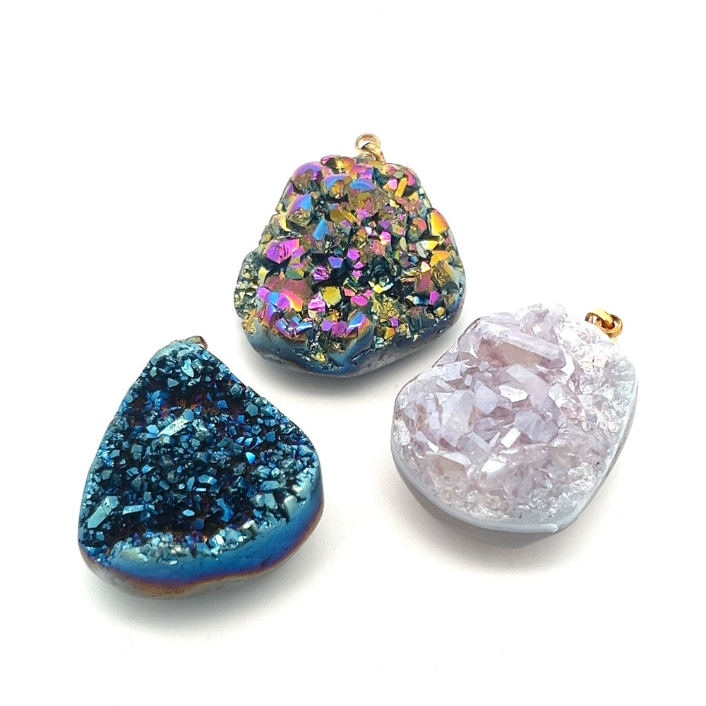 Three exquisite Dazzling Druzy Pendants in blue, multicolored, and pale pink hues, each attached to small gold-plated bails, displayed against a white background.