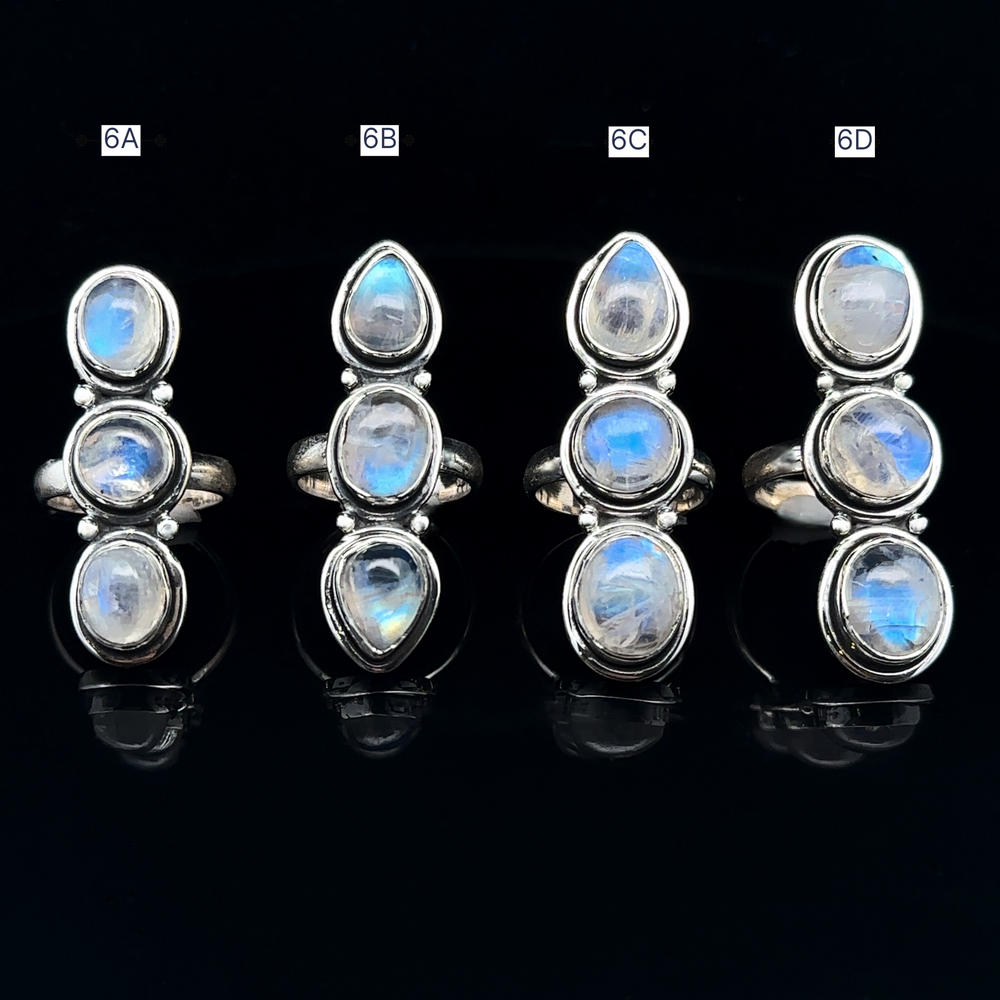 
                  
                    Four Triple Moonstone Rings crafted in sterling silver, exuding goddess energy, are labeled 6A, 6B, 6C, and 6D on a black background.
                  
                