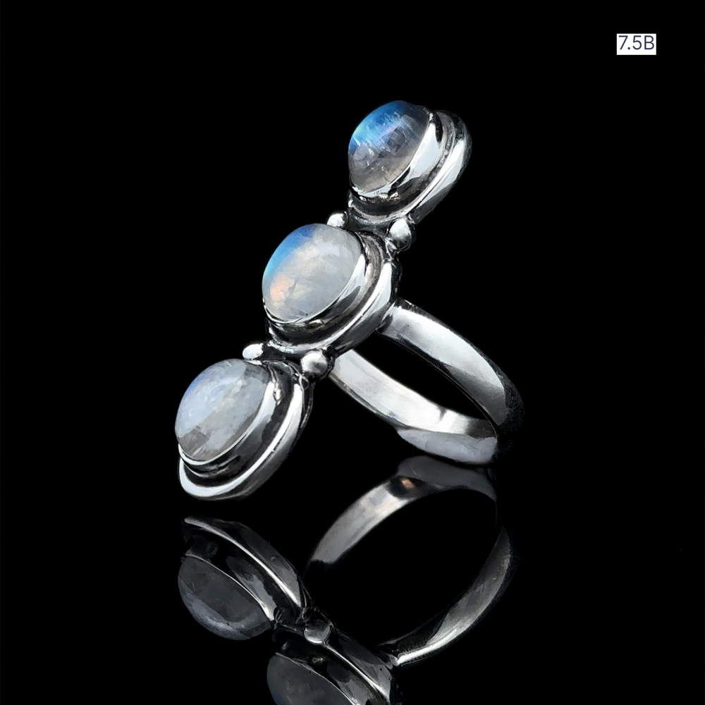 
                  
                    The Triple Moonstone Ring, crafted from sterling silver and featuring three vertically arranged round moonstone gemstones, exudes goddess energy as it is displayed on a black reflective surface.
                  
                