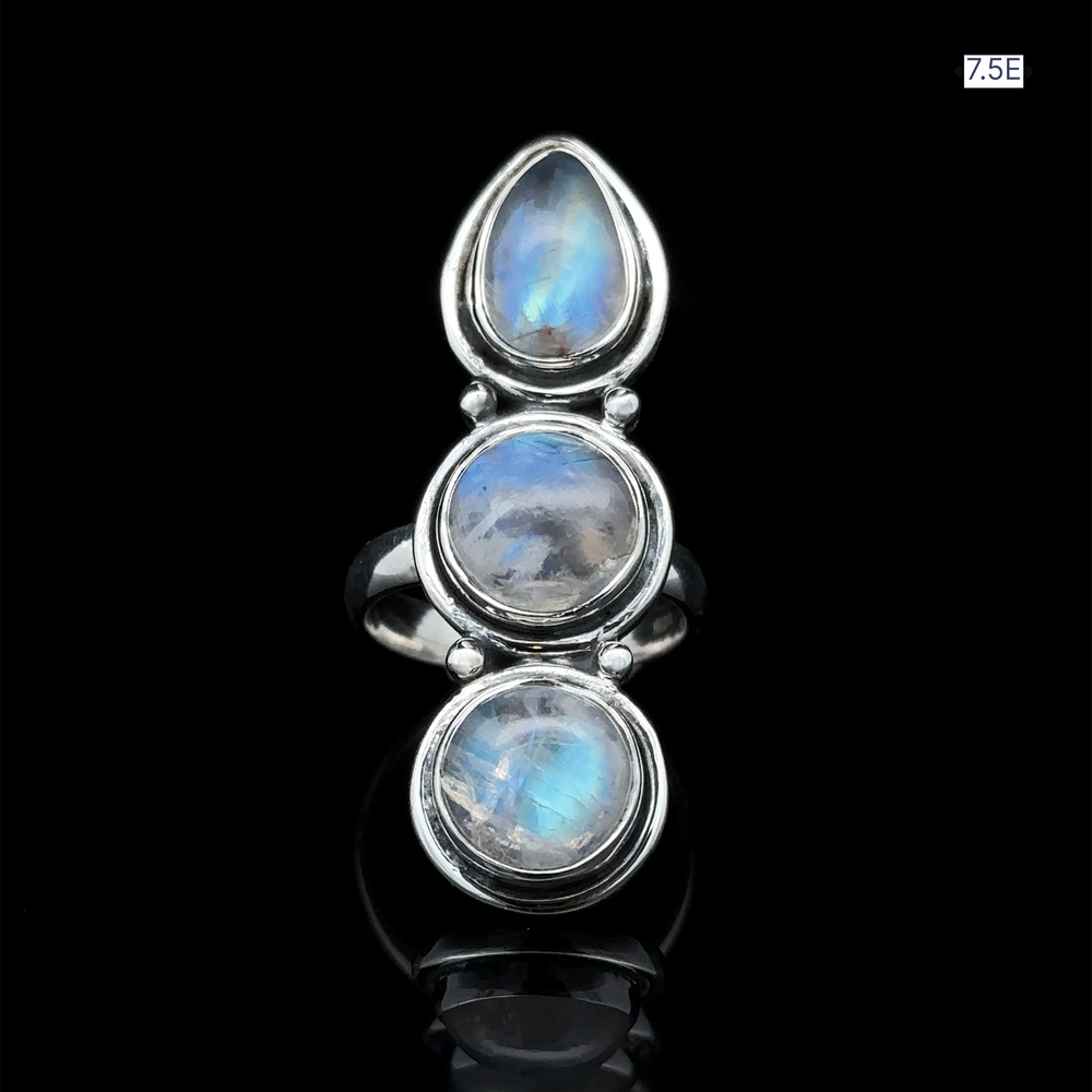 
                  
                    The "Triple Moonstone Ring," crafted from sterling silver and featuring three oval moonstones, radiates goddess energy against a dark background. The size label "7.5E" is positioned in the top right corner.
                  
                