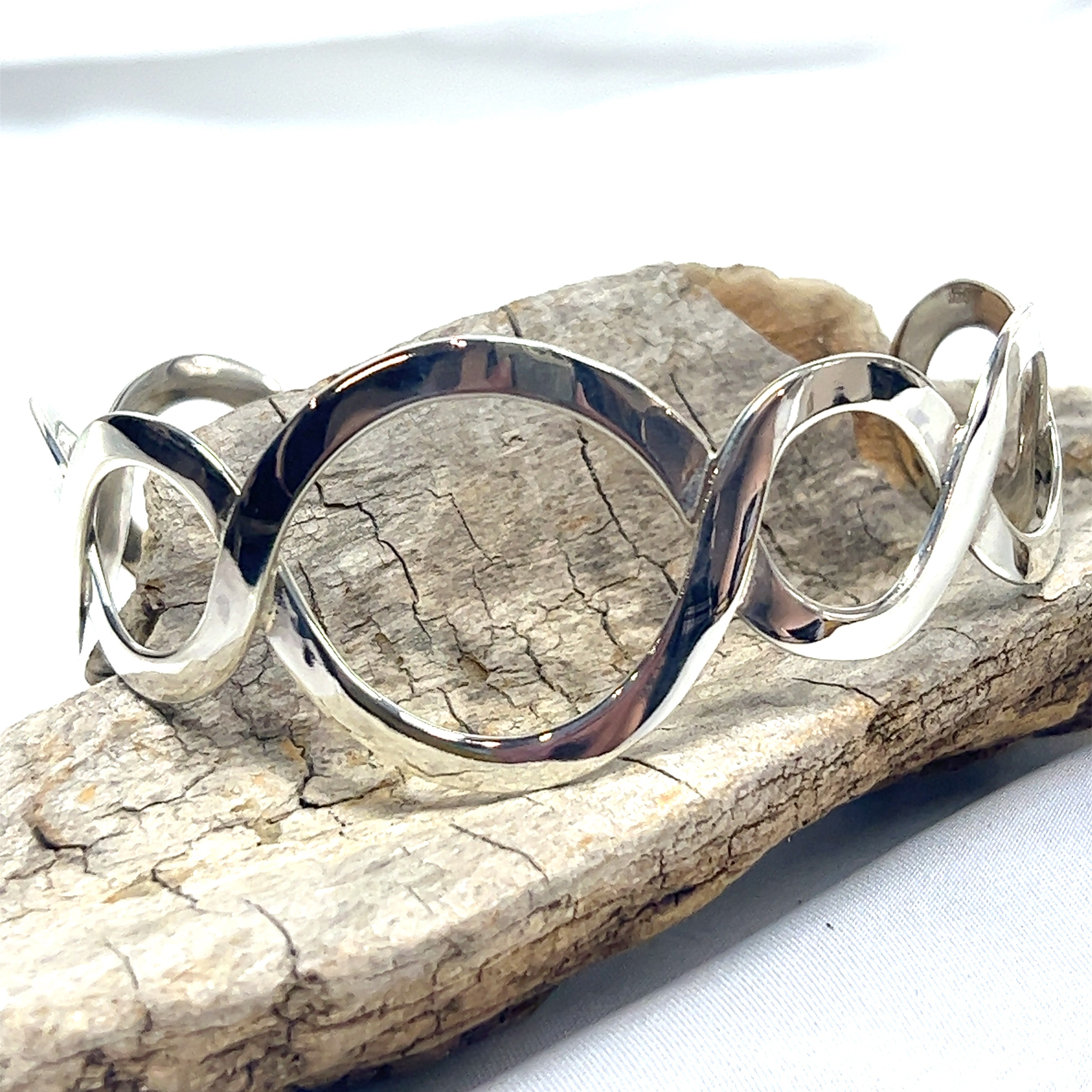 A Super Silver Twisted Graduated Circle Cuff bracelet featuring a graduated circle pattern on a piece of rock.