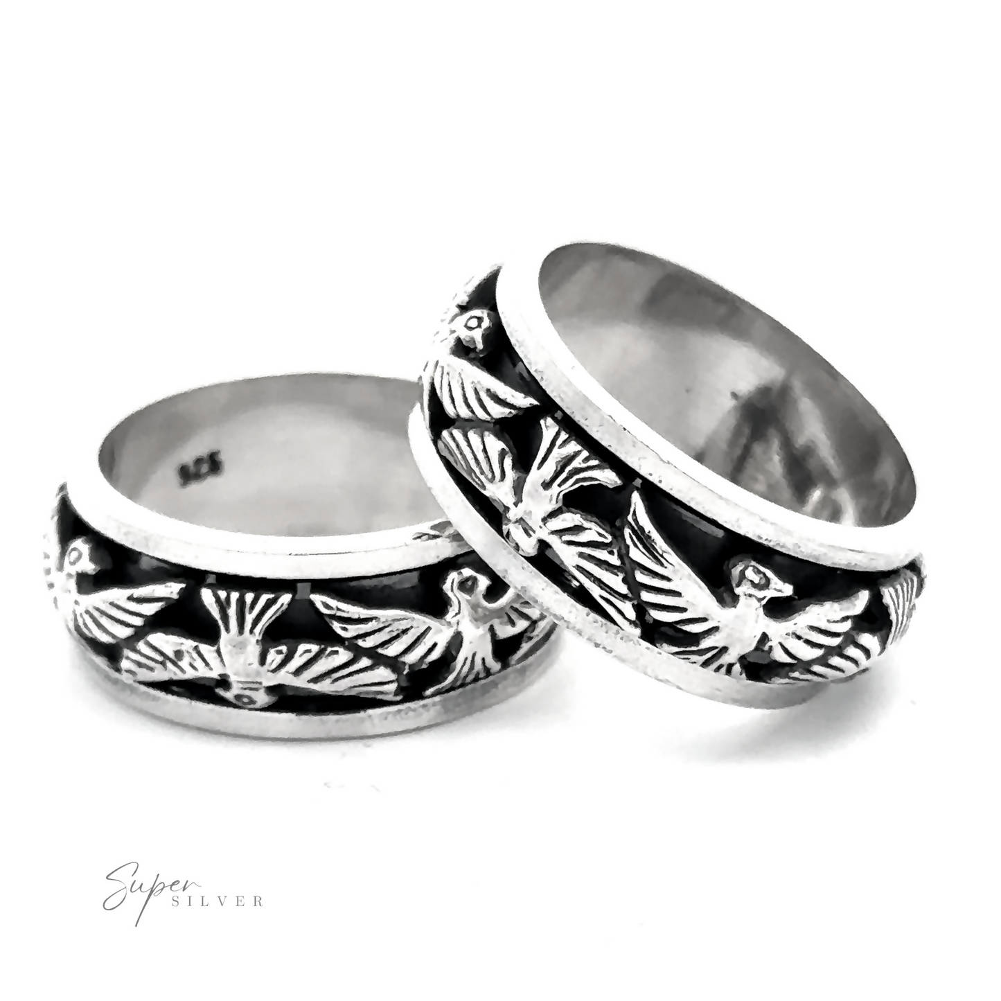 Two Thick Thunderbird Spinner Rings with intricate thunderbird engravings, showing both interior and exterior views. One ring is leaning against the other. The inscription "925" is visible on the inside of both rings.
