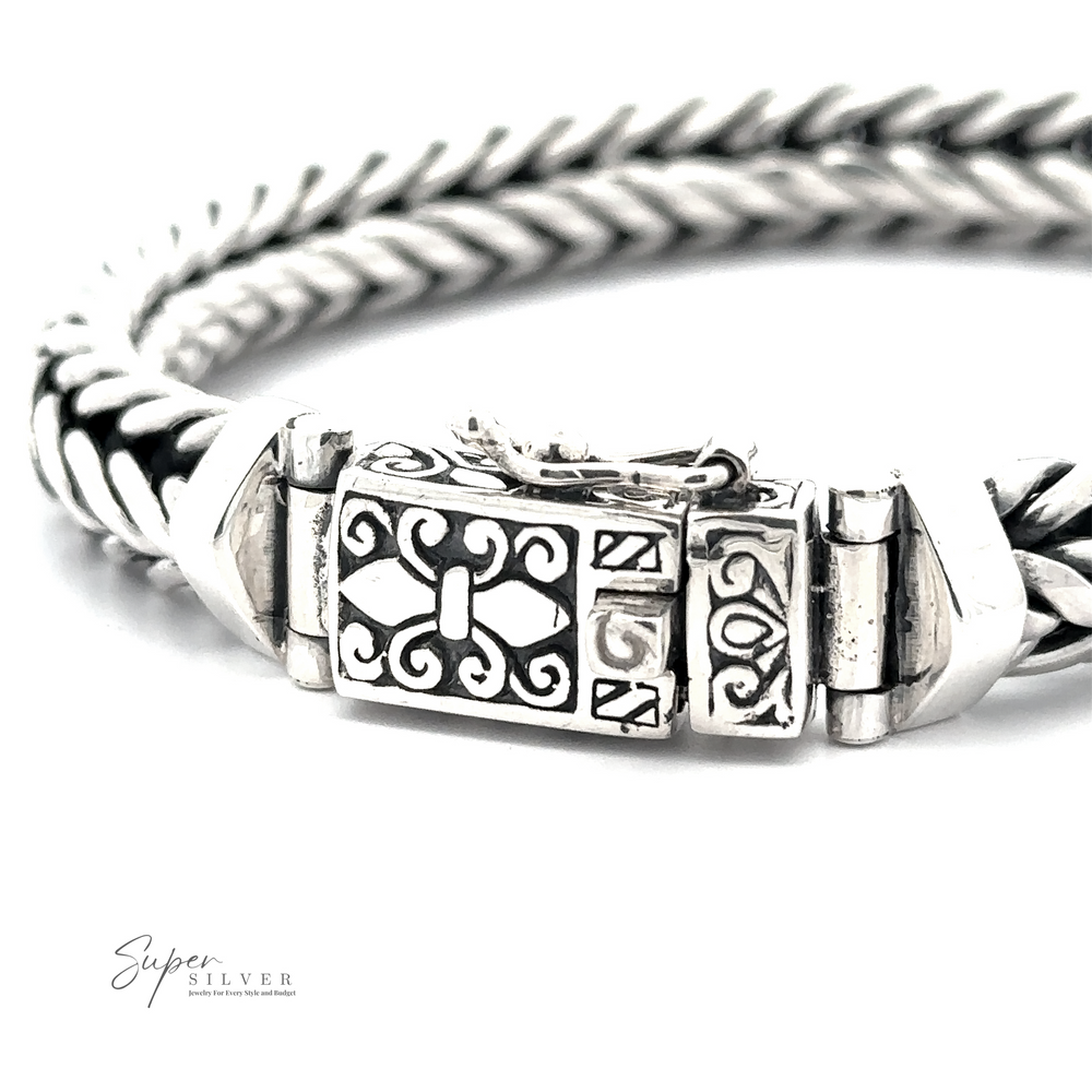 A close-up of a Heavy Braided Bracelet with a braided sterling silver chain and an ornate clasp featuring intricate designs and a fleur-de-lis symbol. The words "Super Silver" are seen in the corner.