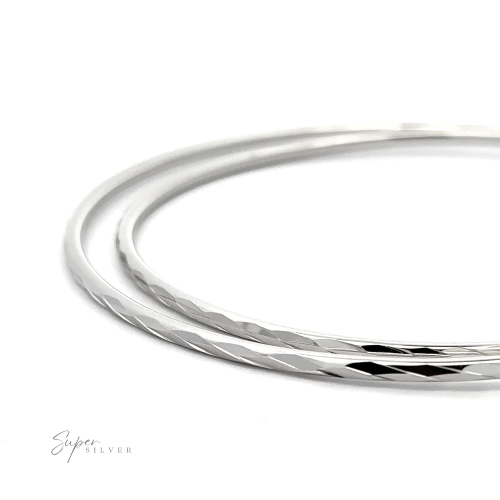 Two thin silver bracelets with a smooth, shiny finish are placed on a white background. The words 