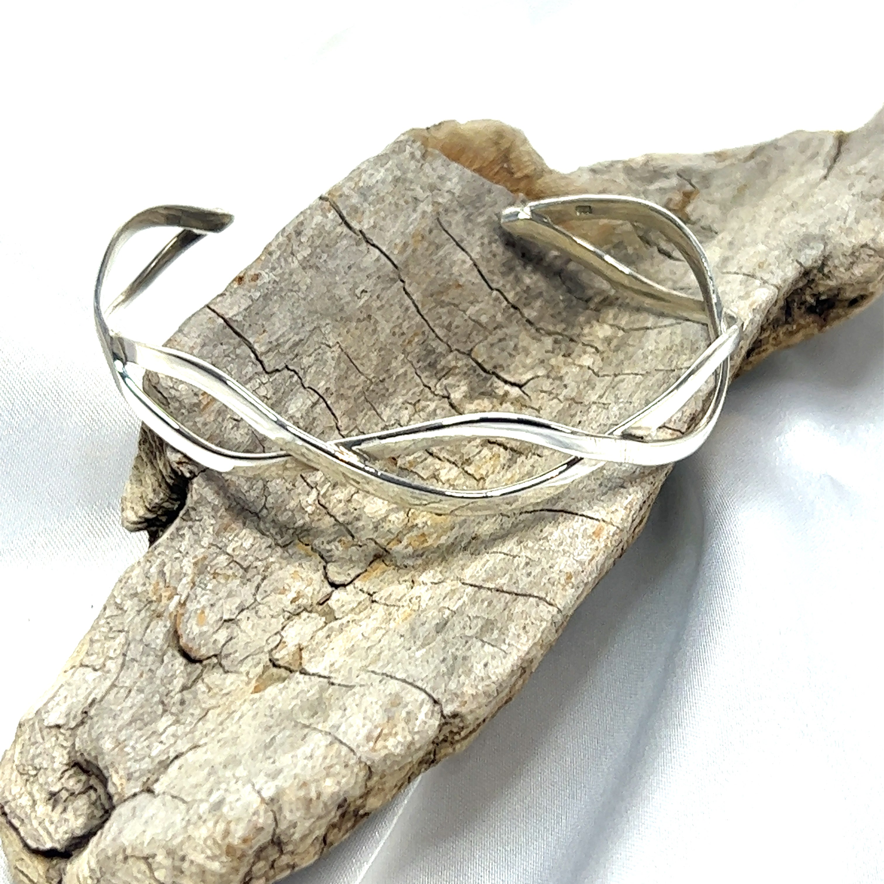 A Super Silver Stylish Twisted Silver Cuff bracelet with a twisting pattern, resting on a piece of wood.