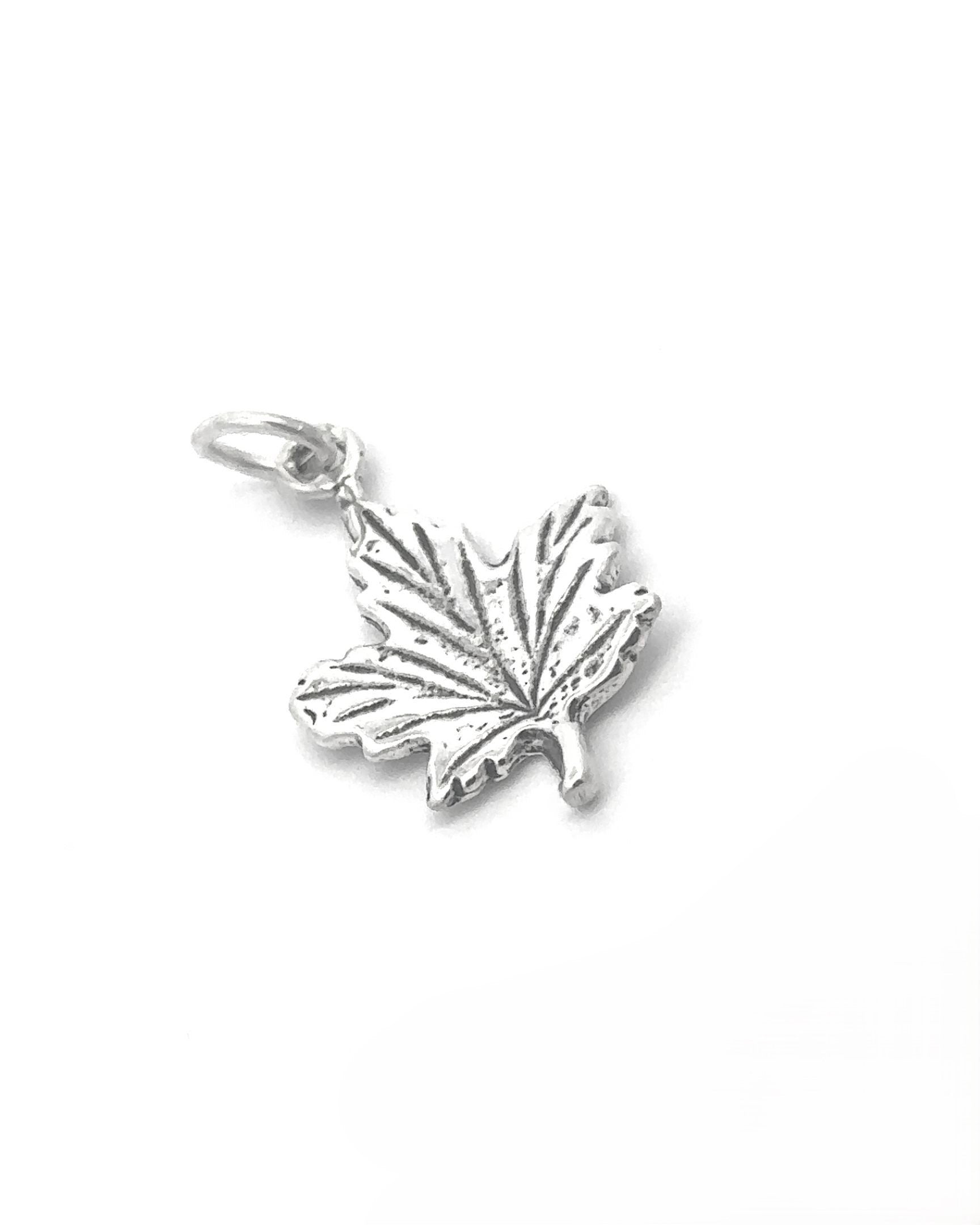 The Tiny Maple Leaf Charm is crafted from sterling silver and features intricate vein patterns along with a small loop for easy attachment, making it the perfect elegant addition to any autumn style.
