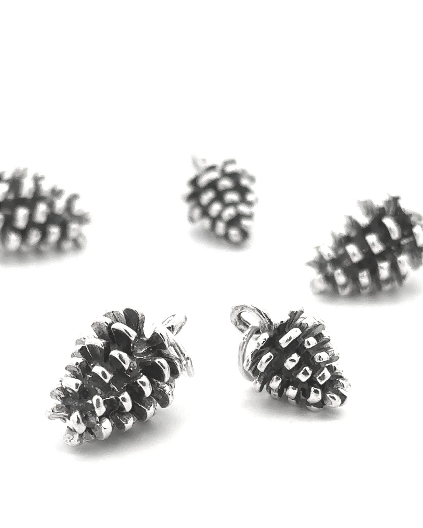 The Pinecone Pendant, made of sterling silver, is scattered on a white surface, making it the perfect accessory for nature lovers.