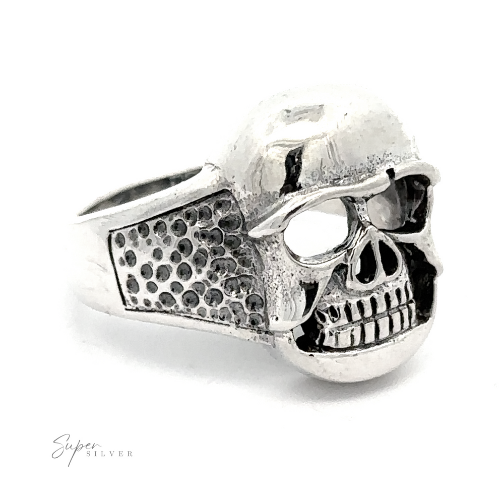 A Skull Statement Ring featuring a detailed skull design with textured patterns on the band and a hollowed-out eye socket on one side; the perfect piece of edgy jewelry.