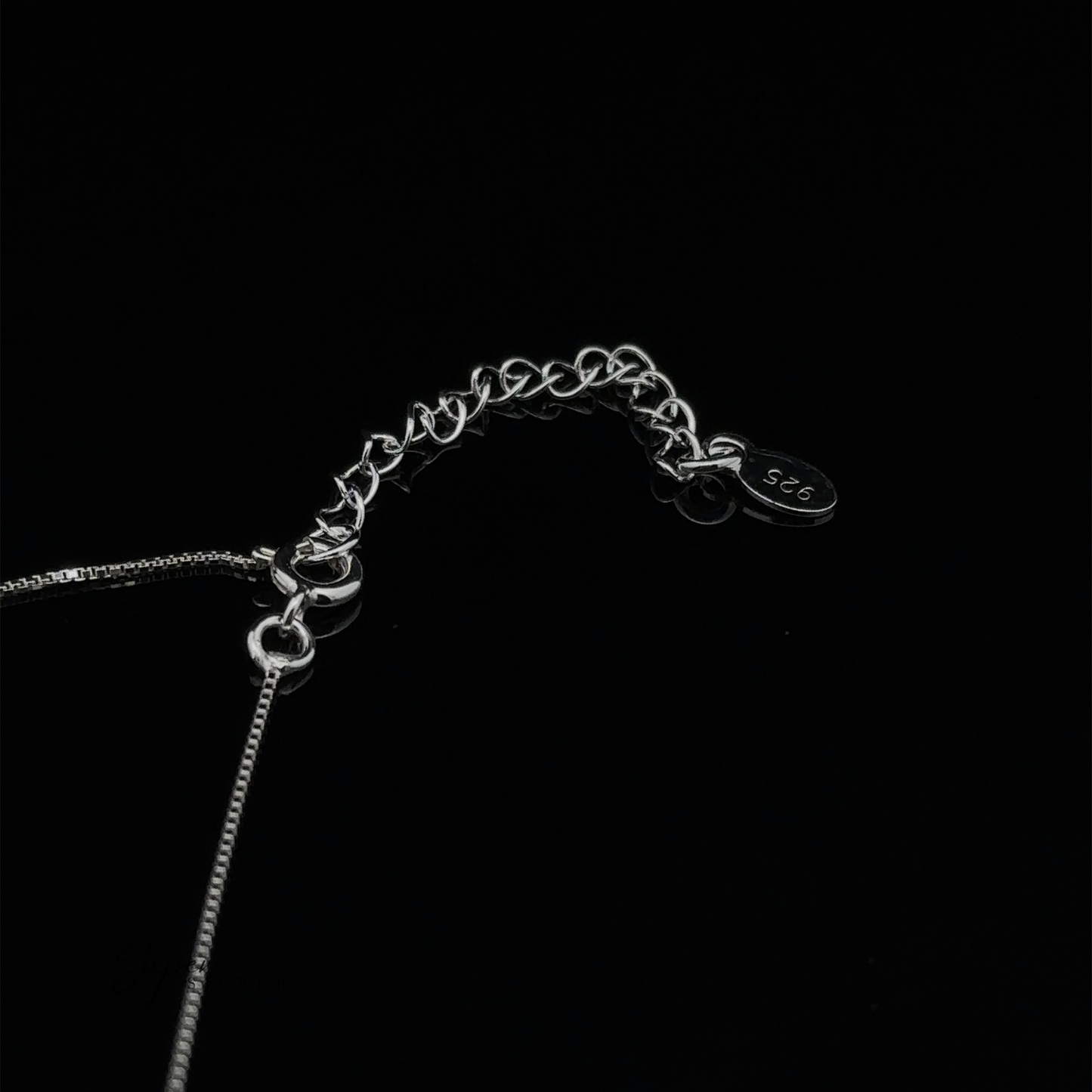 
                  
                    Close-up of a dainty sterling silver Open Heart Lariat Necklace clasp on a black background with a small tag engraved "925.
                  
                