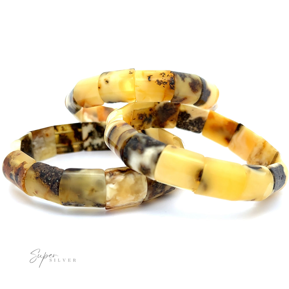 Three beige and brown stone bracelets with a marbled pattern are stacked on a white surface, resembling the elegant Brilliant Butterscotch Amber Stretch Bracelet style. The text 