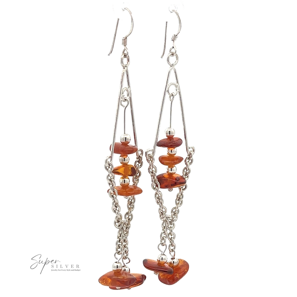 A pair of long, silver, wire-frame **Beaded Amber Tassel Earrings** featuring orange, irregularly shaped beads reminiscent of Baltic amber and hanging chain links in a beaded tassel design, set against a plain white background. Brand name "Super Silver" is visible.
