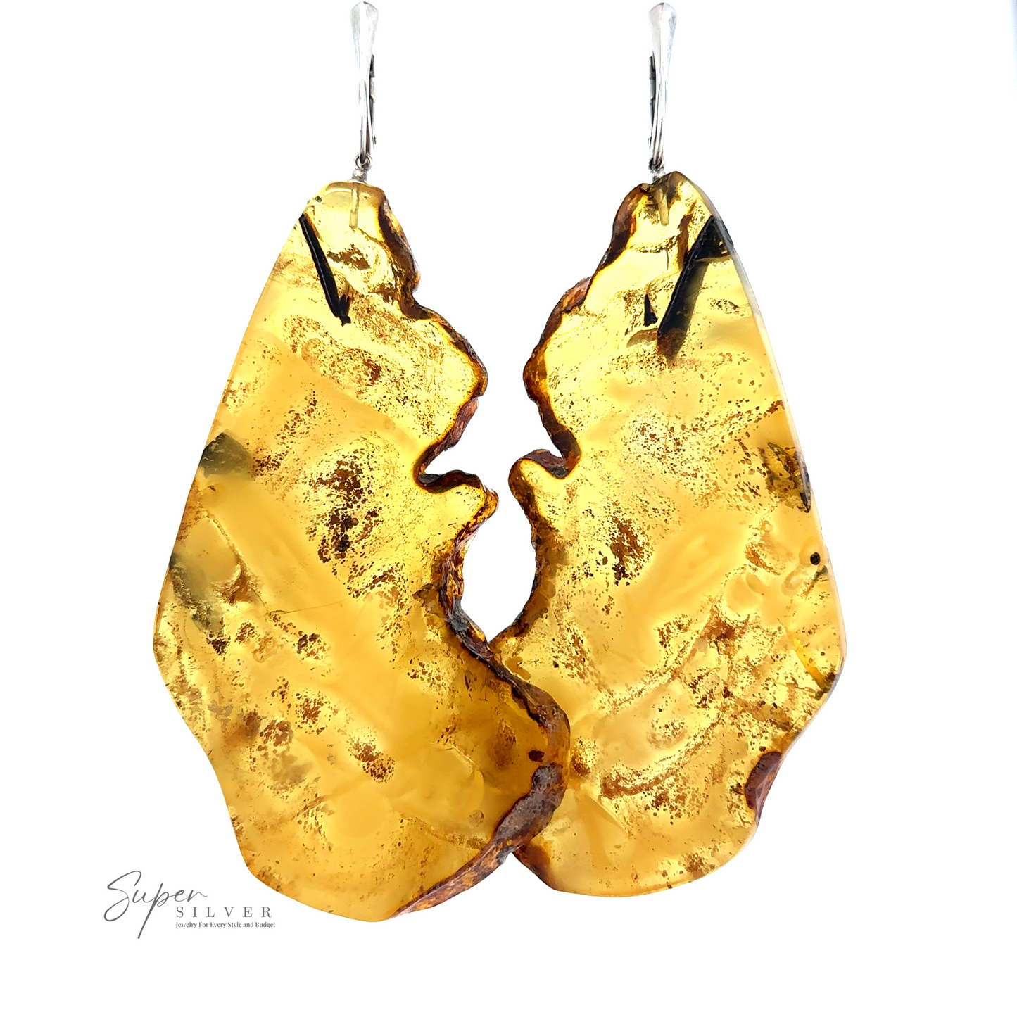 A pair of large, handcrafted Designer Raw Cognac Amber Slab Earrings with an irregular shape, suspended by sterling silver hooks. The logo "Super Silver" is visible in the lower left corner.