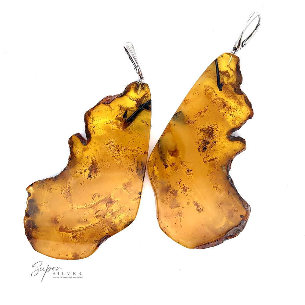 Two handcrafted, Designer Raw Cognac Amber Slab Earrings with silver hooks are displayed against a white background. The amber-colored pieces are beautifully irregular in shape, adding a unique charm to these Sterling Silver Earrings.