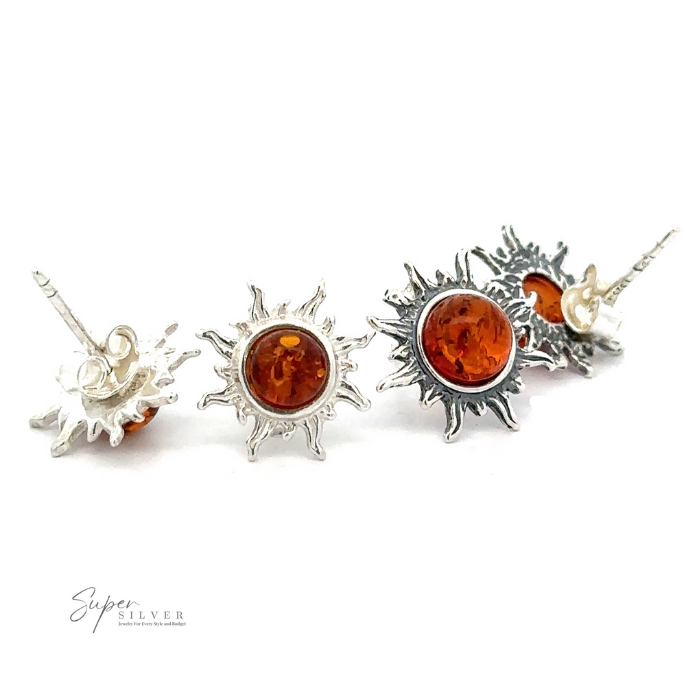 Four silver Brilliant Amber Sun Stud Earrings with Baltic amber stones in the center are displayed on a white background. The logo 