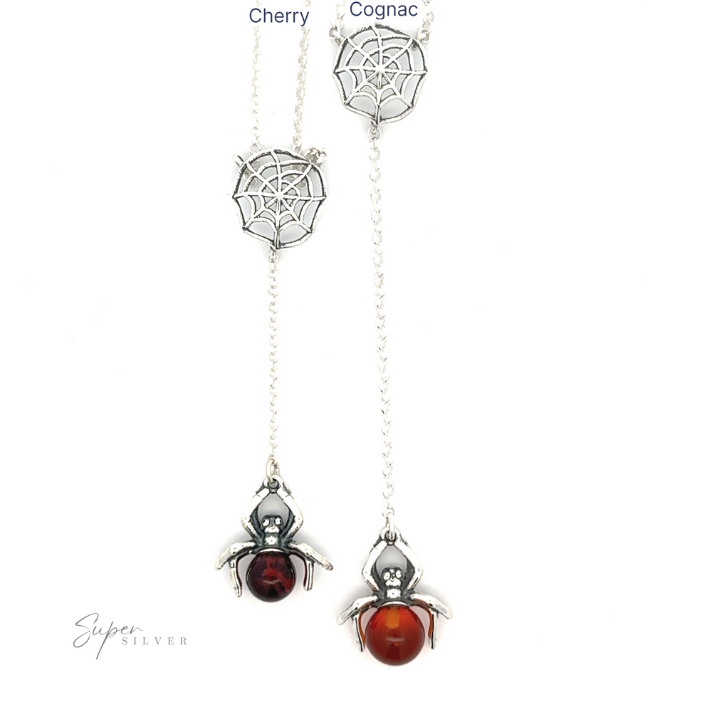 Two silver spider-themed necklaces with web designs exude a witchy vibe. One features a dark red cherry bead, and the other showcases a stunning cognac-colored Baltic amber. Both elegant pieces are branded "Baltic Amber Spider Necklace.