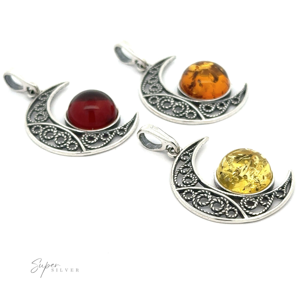 Three Baltic Amber Moon Pendants with intricate designs, each featuring a different colored round gemstone: one red, one Baltic amber, and one yellow. The brand name 