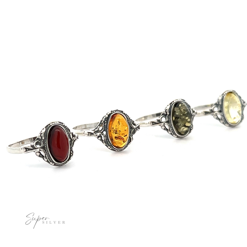 Three ornate sterling silver rings with oval gemstones in red, cognac amber, and green, displayed in a row against a white background.