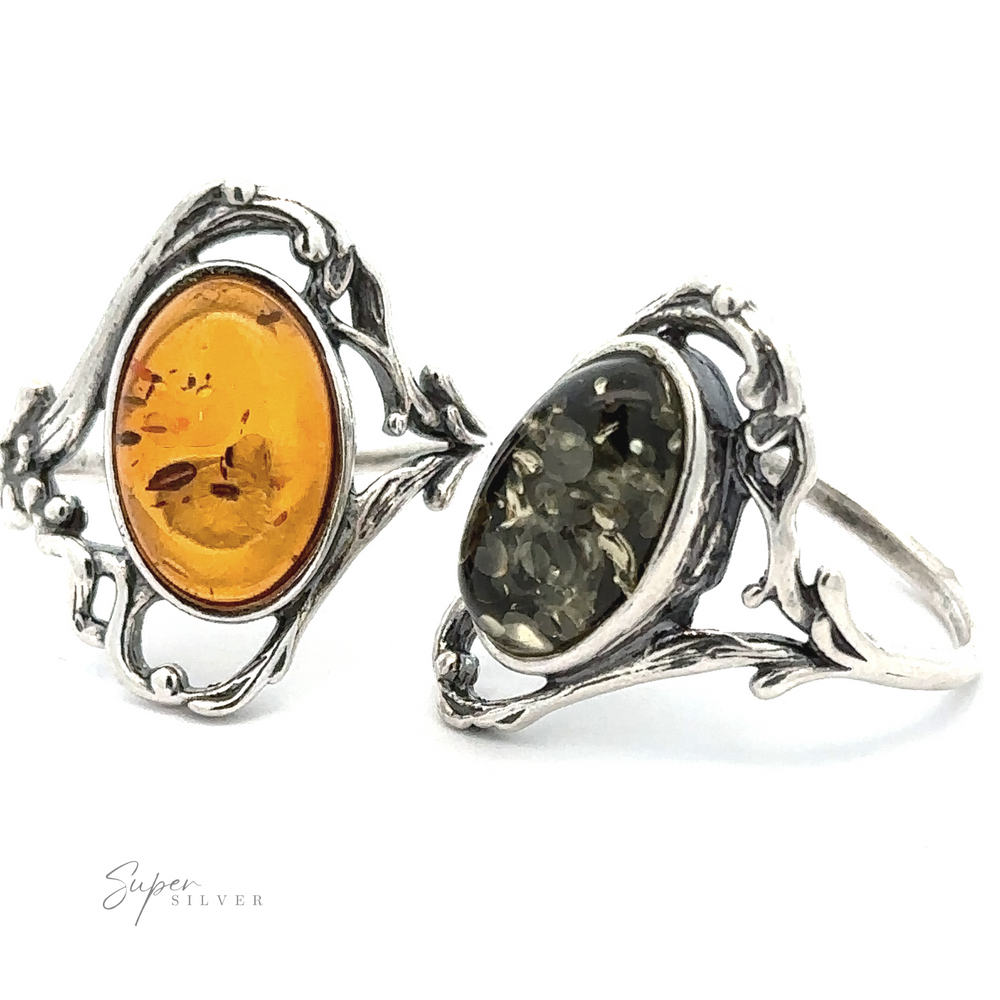 Two ornate silver Amber Rings with Vine Detailing, displaying intricate designs on the sides. One ring features a honey-hued amber, the other a darker stone with embedded particles. The vintage design lends them an antique allure that captivates and enchants.