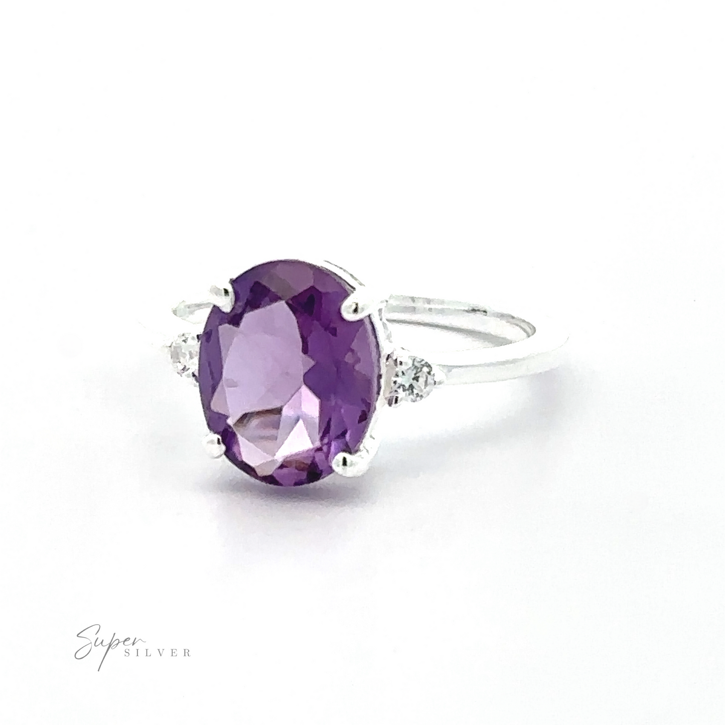 
                  
                    Brilliant Pronged Oval Gemstone Ring featuring a large brilliant oval purple gemstone in a prong setting, flanked by two smaller clear crystals, displayed on a white background.
                  
                