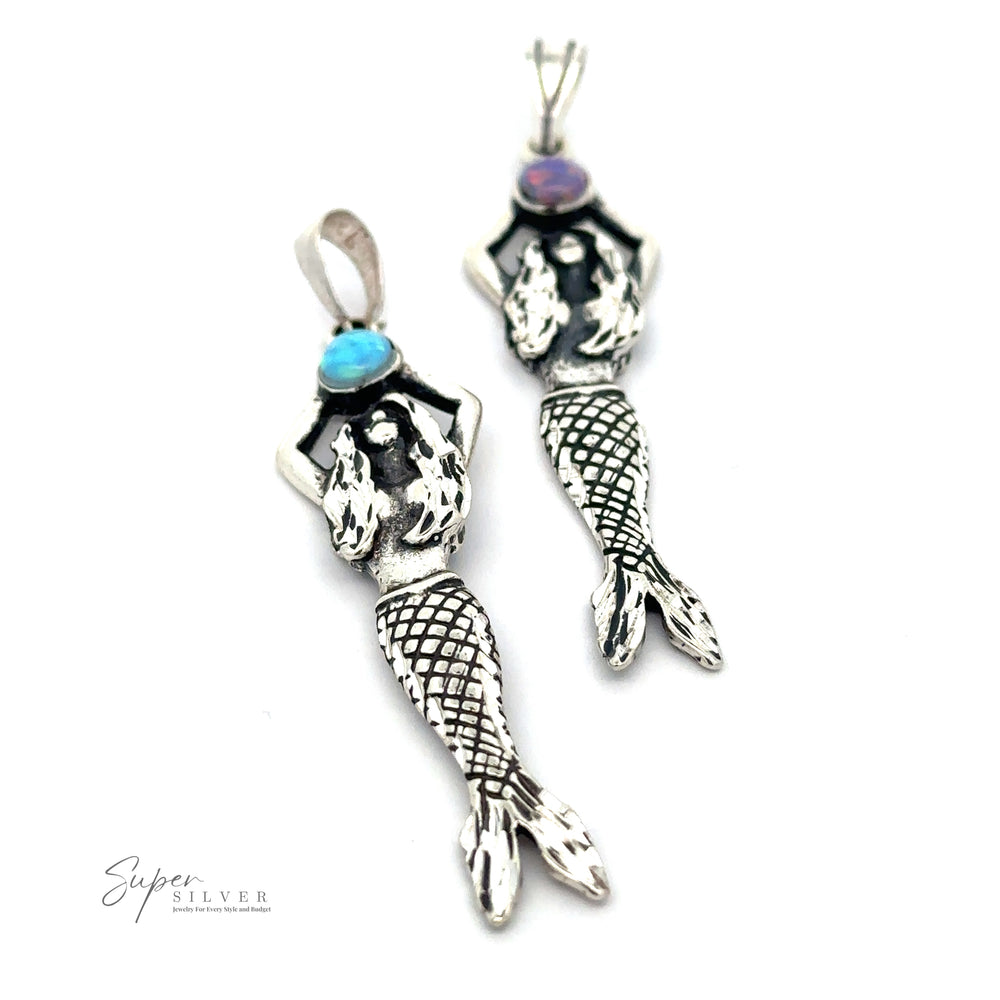 Two Mermaid And Opal Pendants with blue and purple gemstones on the heads, laid on a white background. The brand 