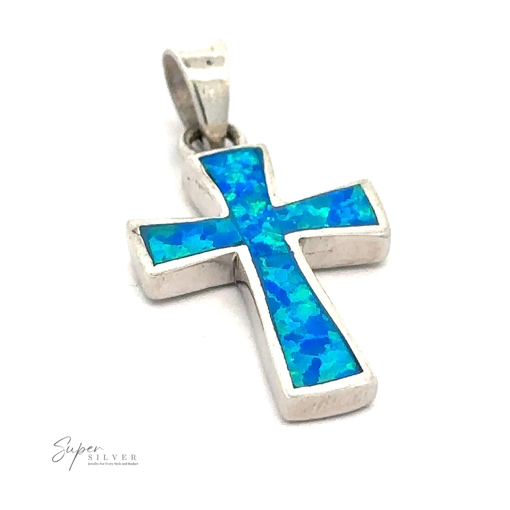 An Opal Cross Pendant features a blue and green mosaic inlay. The background is plain white, and the text "Super Silver" is visible in the bottom left corner. The pendant boasts a rhodium finish, enhancing its elegance and durability.
