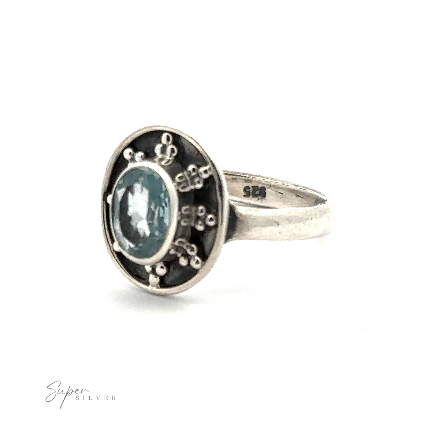 
                  
                    An Oval Gemstone Ring with Ball and Disk Border with a blue gemstone at its center, surrounded by small, intricate designs on a dark background. This vintage-inspired jewelry piece features an inside band inscribed with "925.
                  
                