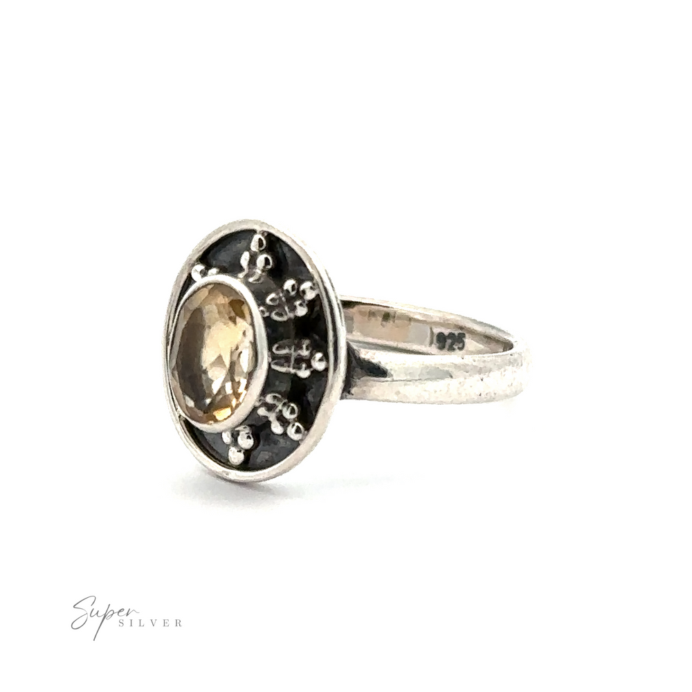 
                  
                    An Oval Gemstone Ring with Ball and Disk Border with an oval-shaped yellow stone set in a dark background, adorned with small silver embellishments. Imprinted with "925" indicating its classic gemstone ring composition, this piece exudes vintage-inspired jewelry charm.
                  
                