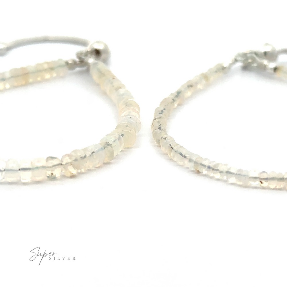 Close-up of two looped beaded earrings made of small, semi-transparent stones. The logo 