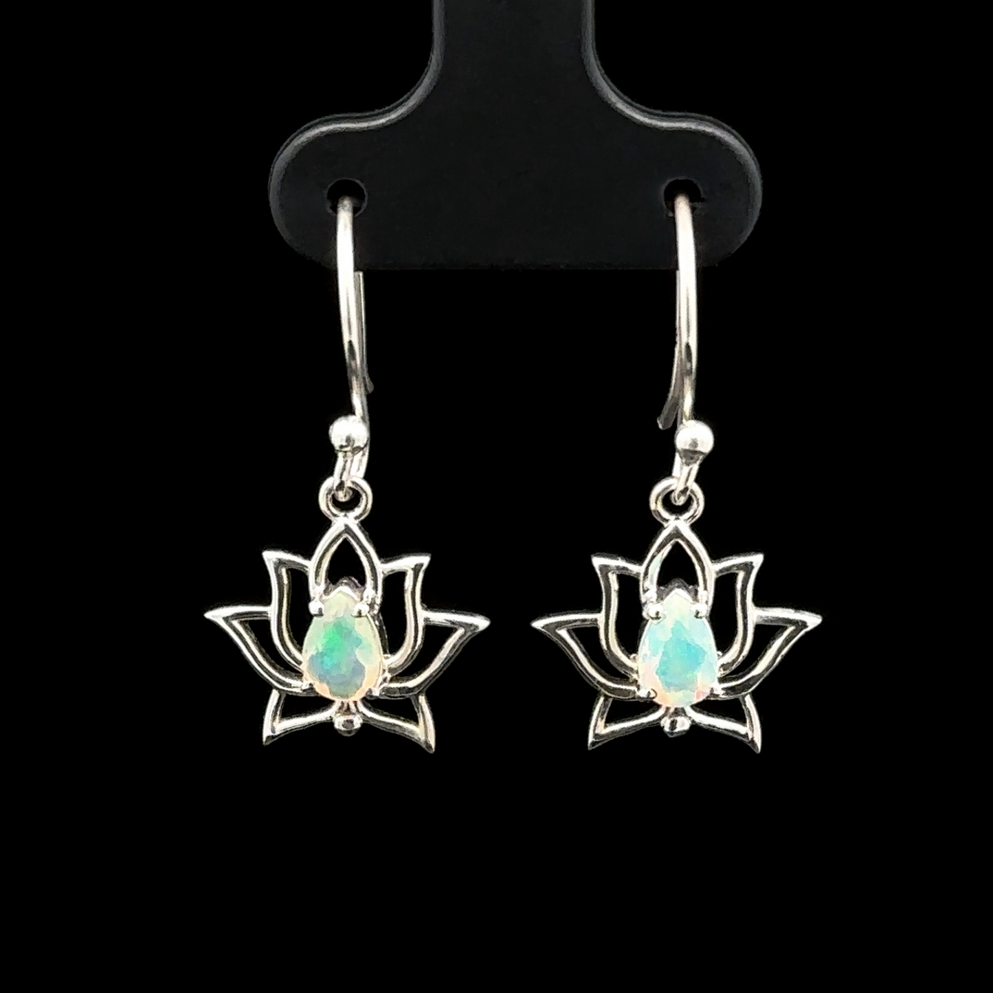 
                  
                    The Ethiopian Opal Lotus Earrings elegantly showcase sterling silver lotus flowers adorned with opal gemstones, all set against a captivating black backdrop and suspended delicately from hooks.
                  
                