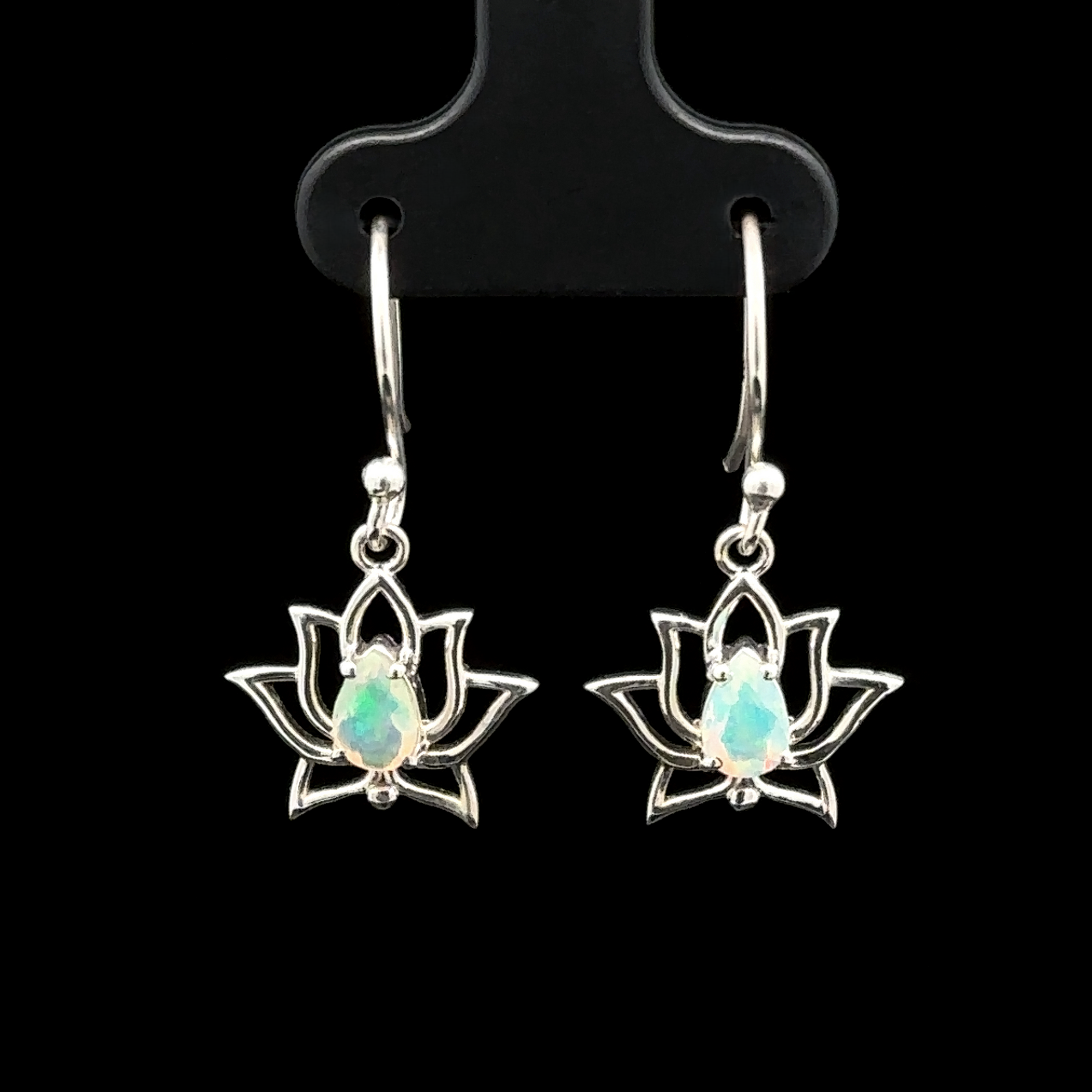 The Ethiopian Opal Lotus Earrings elegantly showcase sterling silver lotus flowers adorned with opal gemstones, all set against a captivating black backdrop and suspended delicately from hooks.