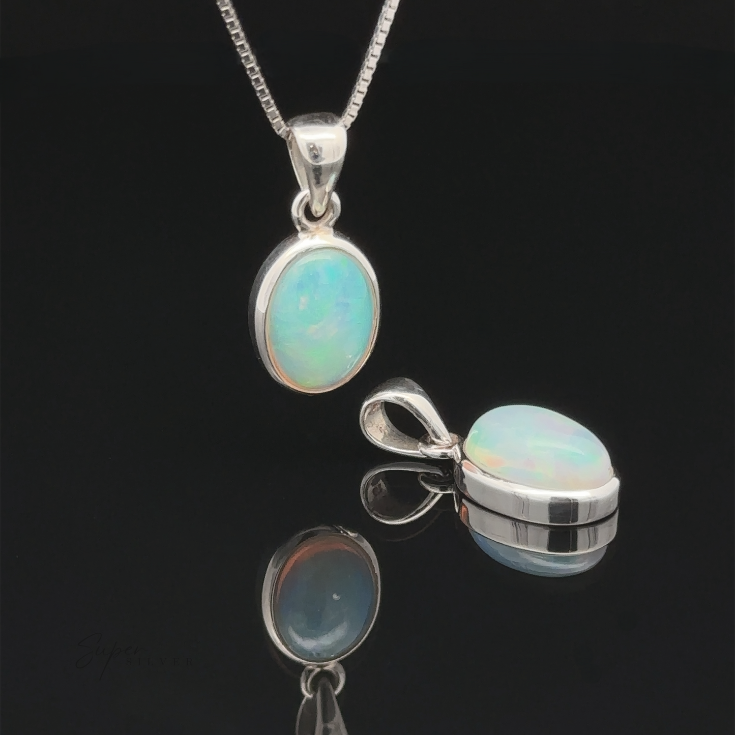 An Oval Ethiopian Opal Pendant on a sterling silver chain is displayed alongside a loose matching piece, both highlighting their subtle elegance on a reflective black surface.