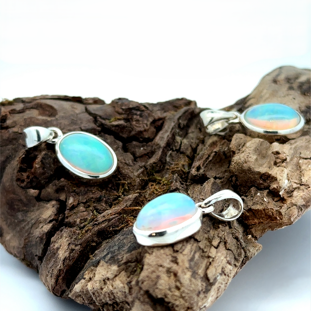 
                  
                    Three Oval Ethiopian Opal Pendants with sterling silver settings are elegantly displayed on a piece of driftwood, embodying a minimalist style.
                  
                