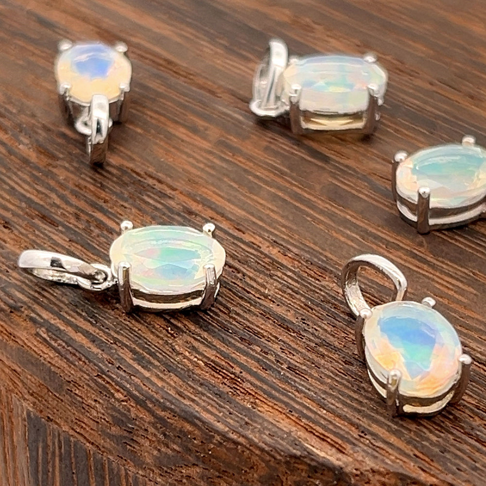 
                  
                    Five Tiny Oval Pronged Ethiopian Opal Pendants, crafted from sterling silver, elegantly showcase their minimalist design with oval Ethiopian opal gemstones on a wooden surface.
                  
                