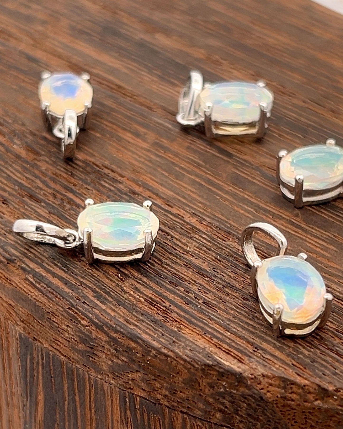 
                  
                    Five Tiny Oval Pronged Ethiopian Opal Pendants, crafted from sterling silver, elegantly showcase their minimalist design with oval Ethiopian opal gemstones on a wooden surface.
                  
                