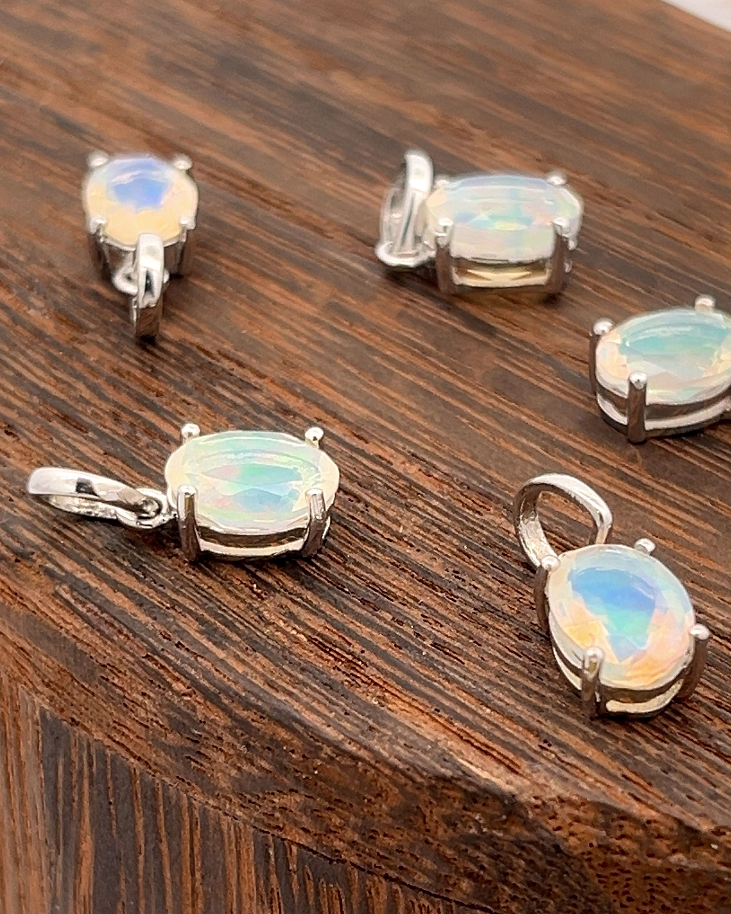 Five Tiny Oval Pronged Ethiopian Opal Pendants, crafted from sterling silver, elegantly showcase their minimalist design with oval Ethiopian opal gemstones on a wooden surface.