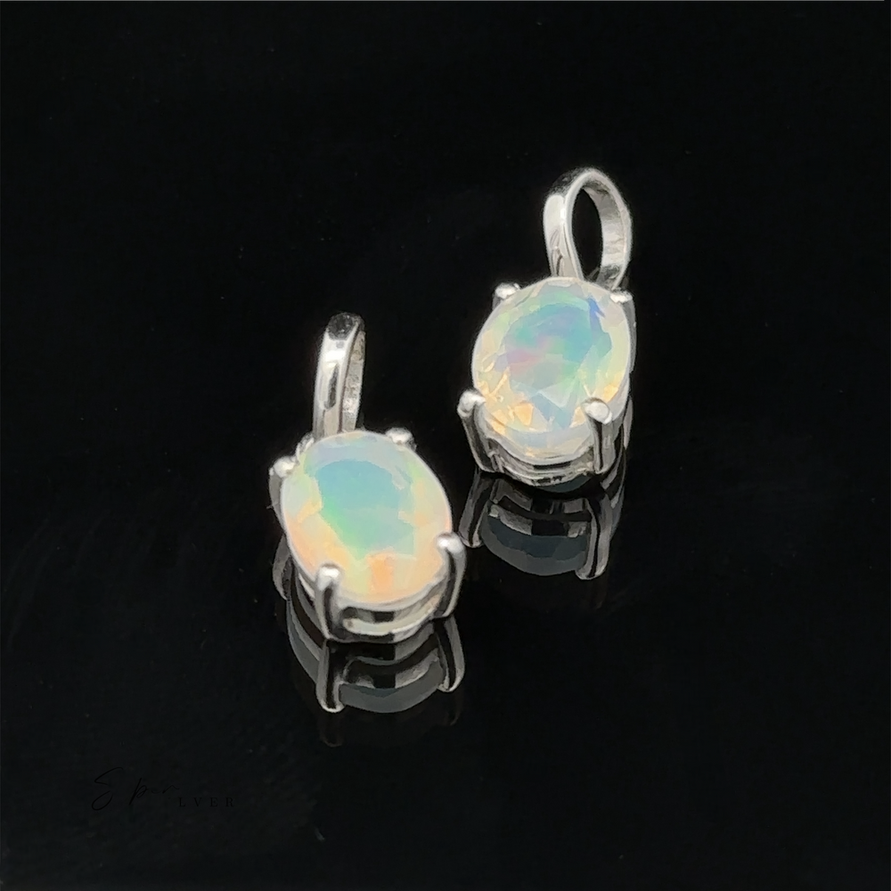 Two Tiny Oval Pronged Ethiopian Opal pendants set in sterling silver, resting on a reflective black surface.