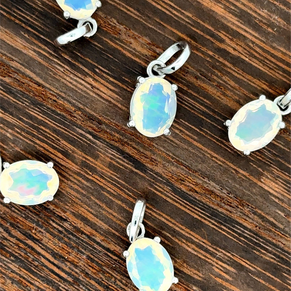 
                  
                    Five Tiny Oval Pronged Ethiopian Opal Pendants, crafted with Ethiopian opal and set in sterling silver, are elegantly arranged on a wooden surface.
                  
                