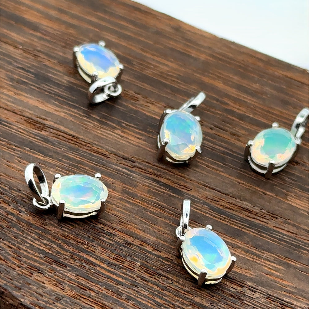 Five Tiny Oval Pronged Ethiopian Opal Pendants, each crafted with Ethiopian opal set in sterling silver, are elegantly displayed on a wooden surface.