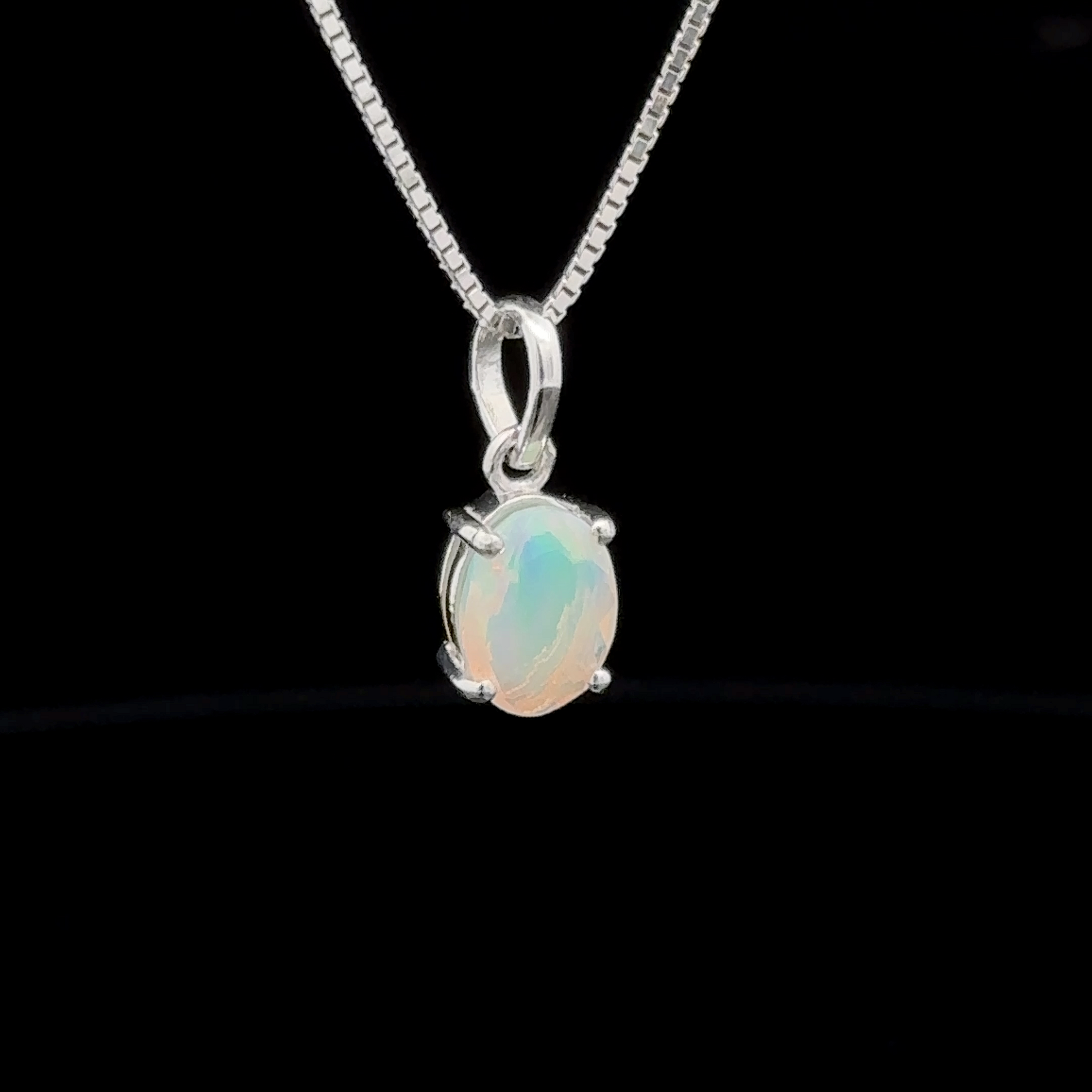 A sterling silver necklace showcasing a Tiny Oval Pronged Ethiopian Opal Pendant, elegantly set against a black background.